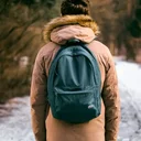 Individual trekking in a winter landscape, bundled up in a brown jacket and equipped with a green backpack.